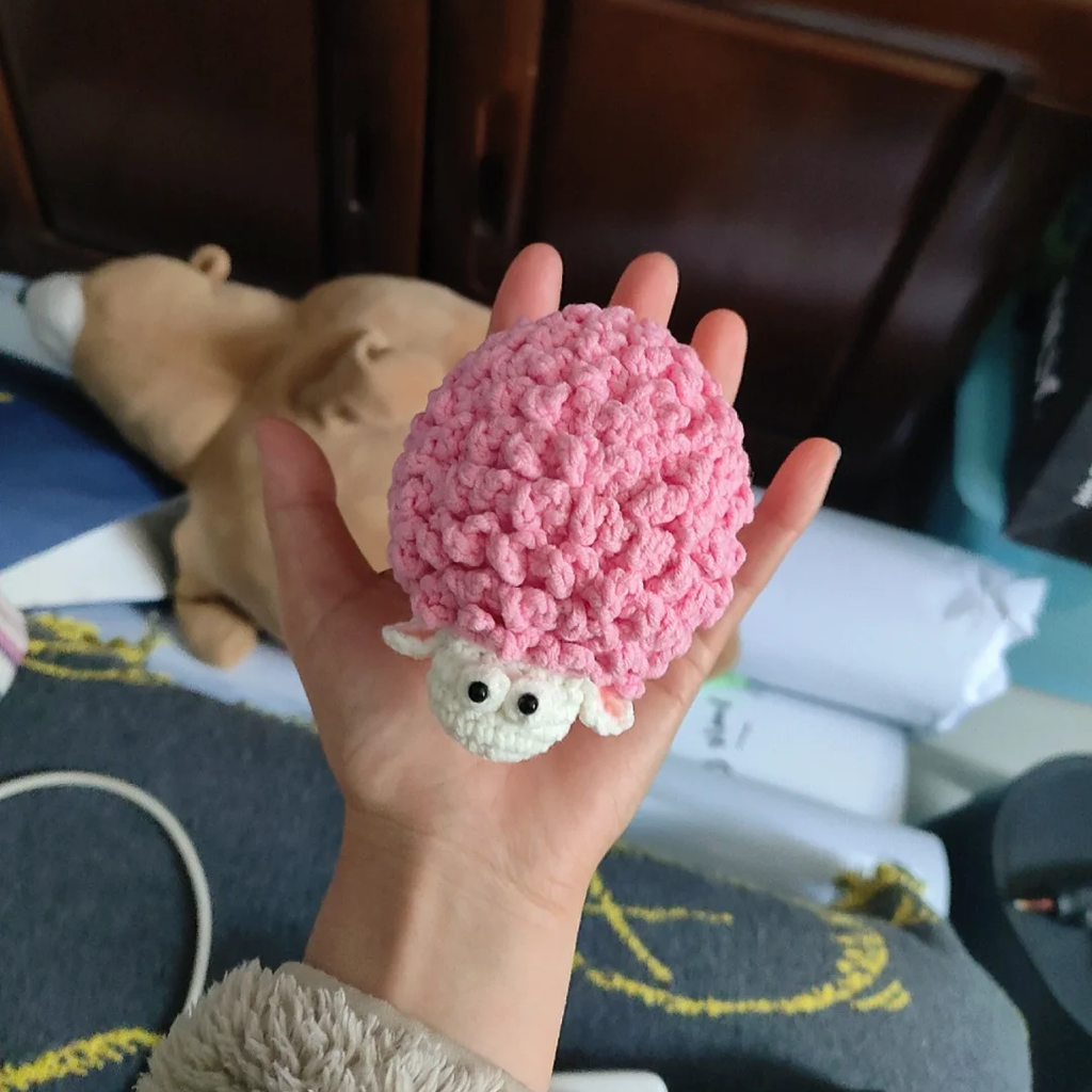 Top view of a small pink sheep amigurumi showing plush wool curls and white face
