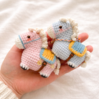 Pink and pale blue tiny crochet horses with saddle blankets and bridle, held in a hand