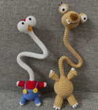 Two crocheted long-neck funny animals in beige and white with red and blue outfit