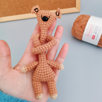 Tan-colored long-neck crochet animal toy with small ears and winding neck held in a hand