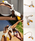 White long-neck crochet goose with yellow beak and feet wrapped around a brown bag strap