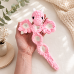 Pink and white handmade popping dragon crochet toy with wings open, held in a hand
