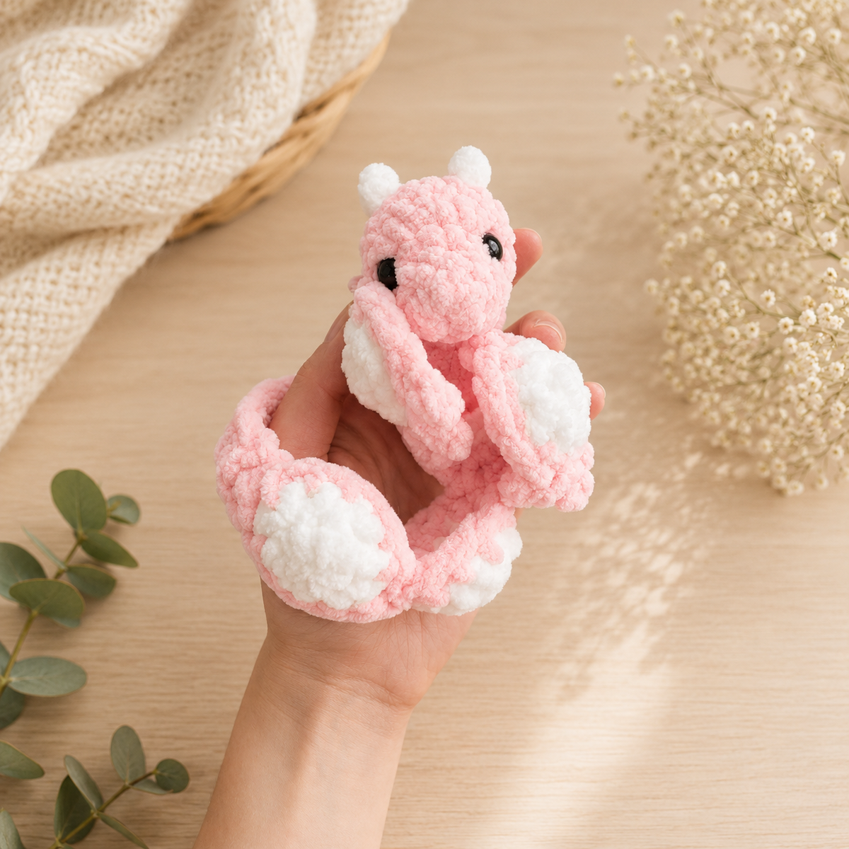 Interactive pink crochet dragon rolled into a compact ball inside a hand